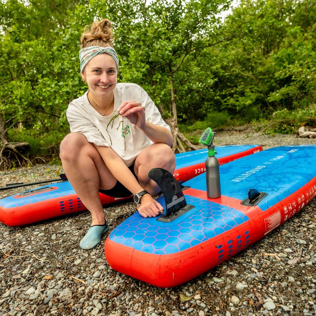 A woman is picking out lake weed from her paddleboard.