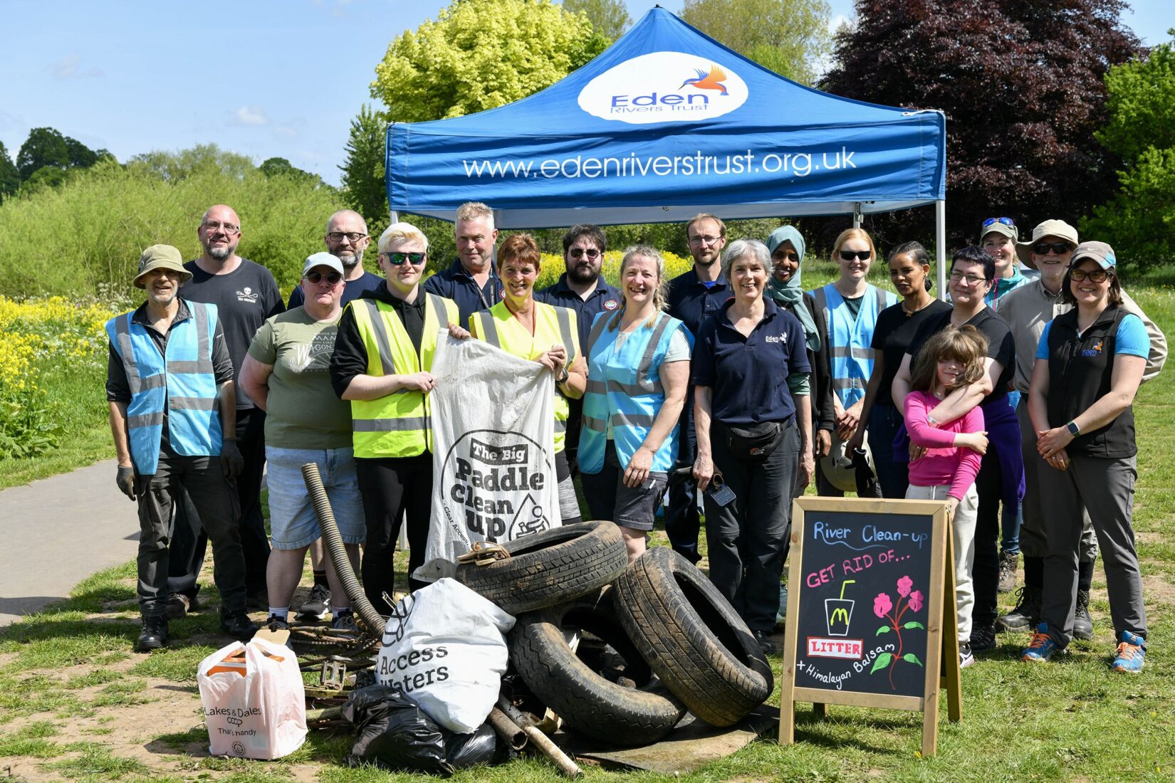 Large group of adults stood smiling, behind a mound of full bin bags, types and other rubbish