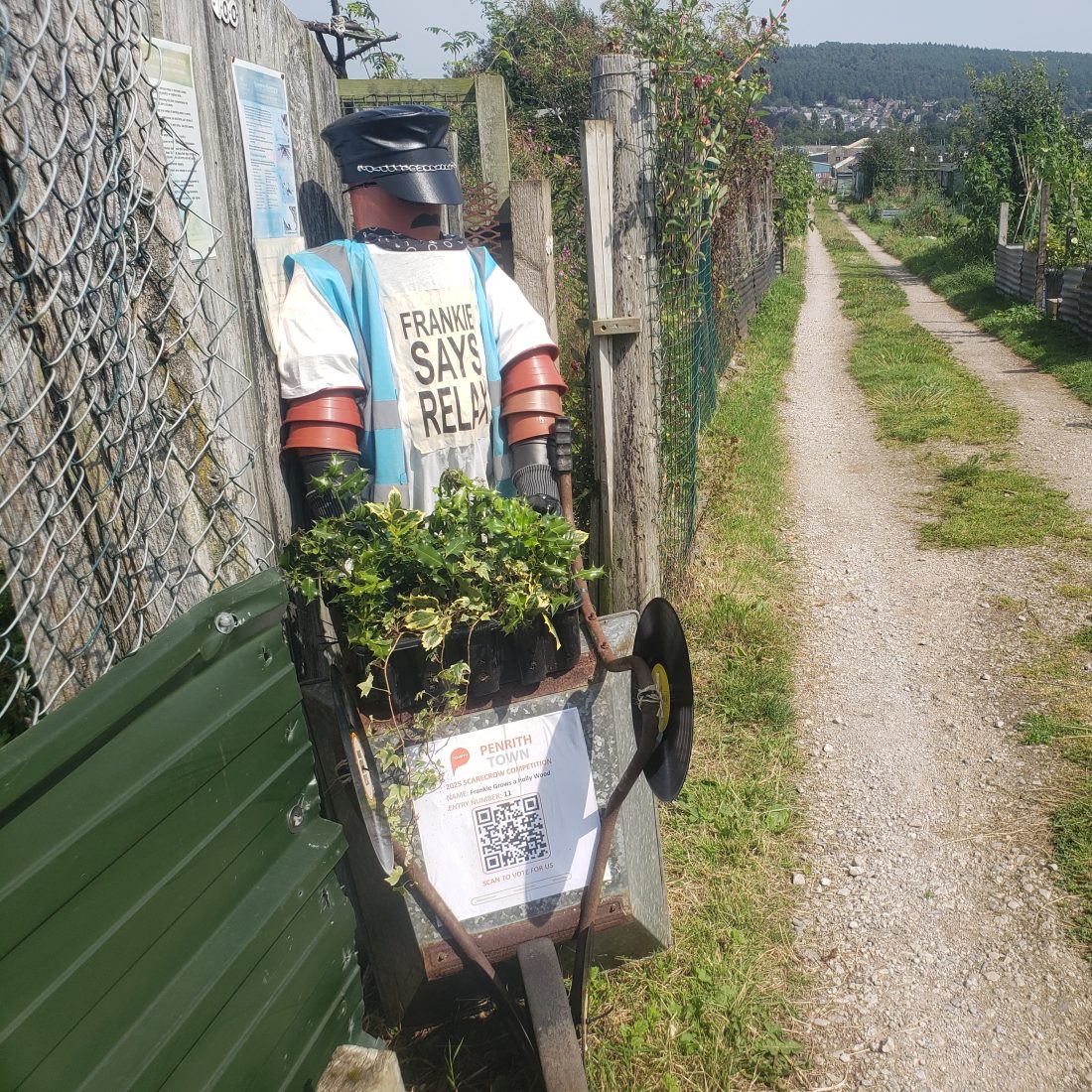 A picture of the ERT entry for the Penrith scarecrow competition. Titles Frankie grows a holly wood it is a depiction of a member of the band Frankie Goes to Hollywood constructed from flower pots, holding a wheelbarrow and wearing a t shirt than reads: 