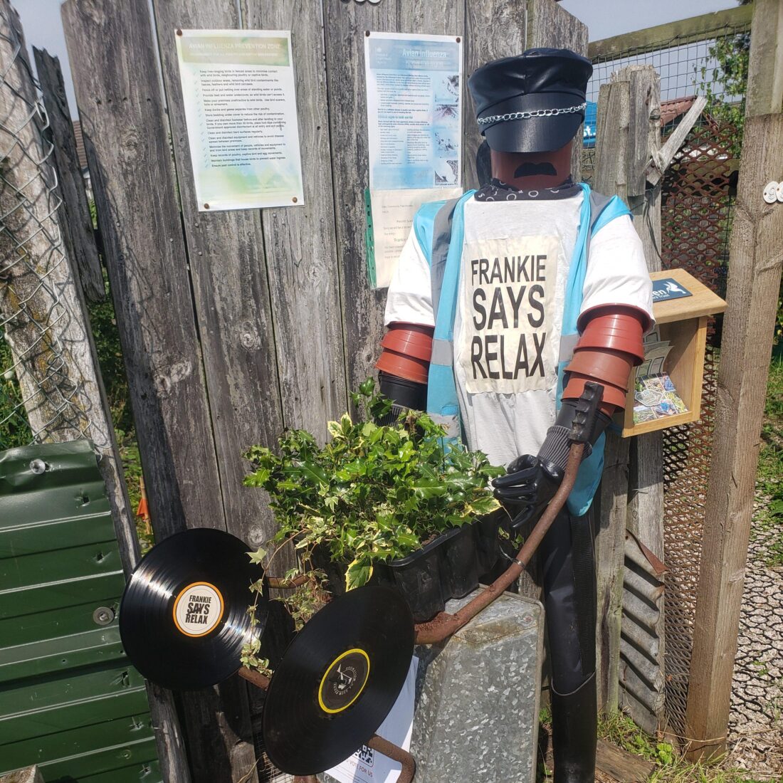ERT scarecrow made of flower pots and holding a wheelbarrow standing outside the entrance to the Penrith community tree nursery.