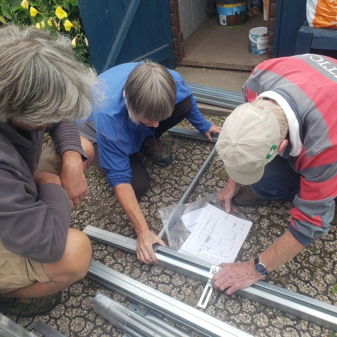A group of volunteers around a box of polytunnel construction items and reading instructions on how to assemble them.