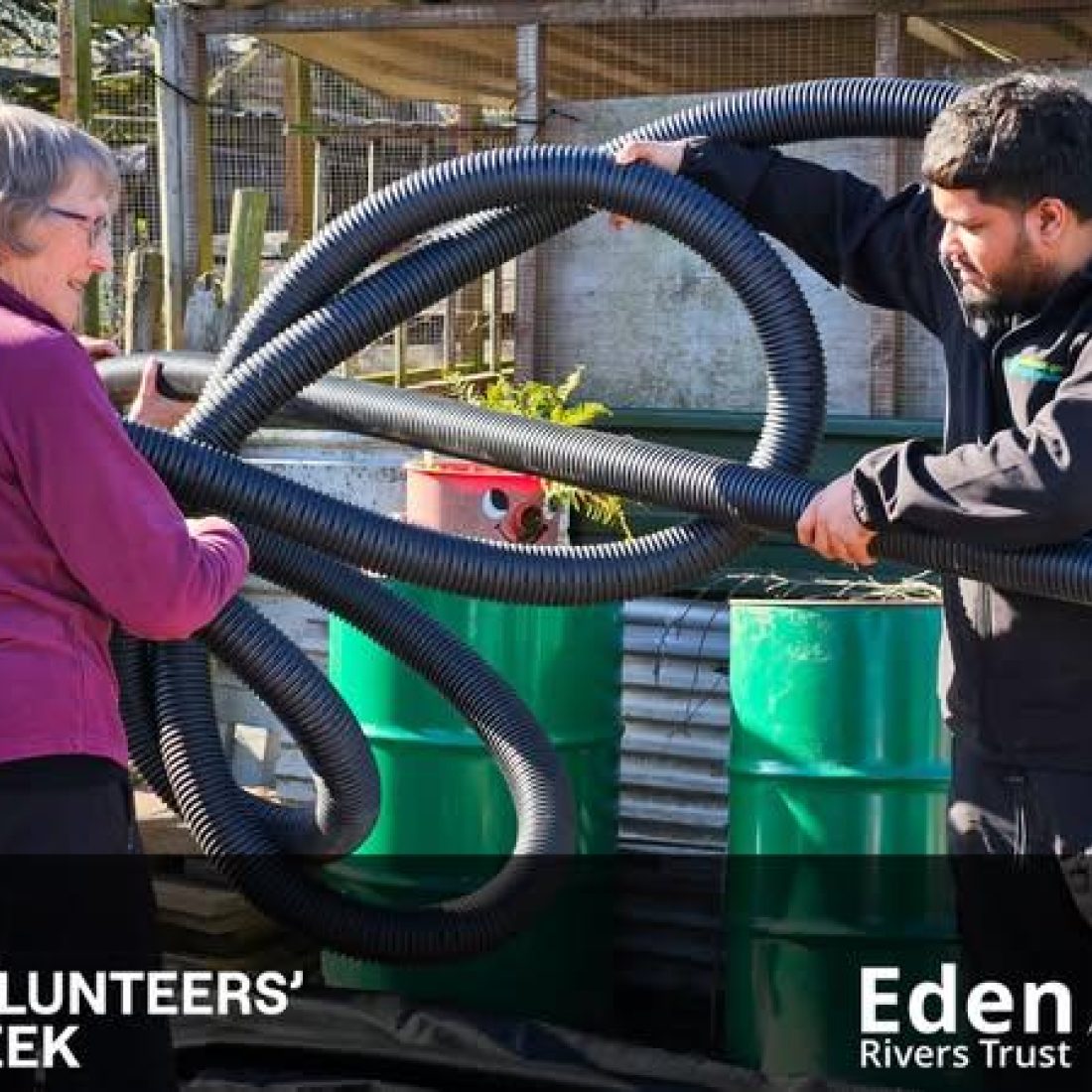 Two volunteers untangling a large plastic section of water pipe which will be seated in a ditch to create a 'French drain'.