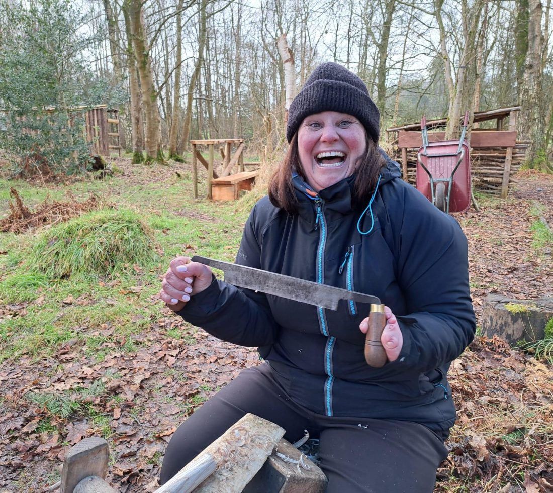 A volunteer sat on a shaving horse holding and learning green woodworking skills.