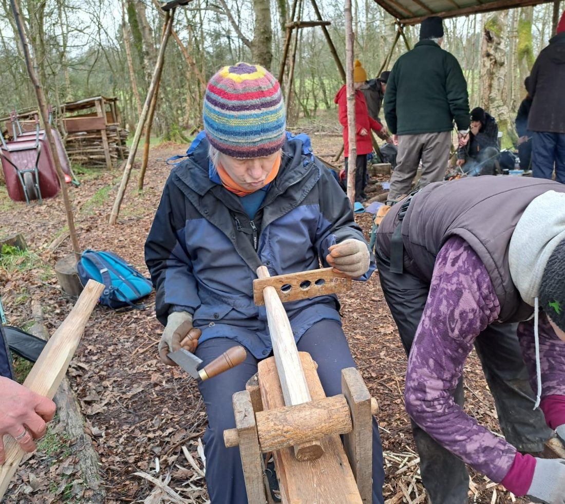A volunteer sat on a shaving horse holding and learning green woodworking skills.