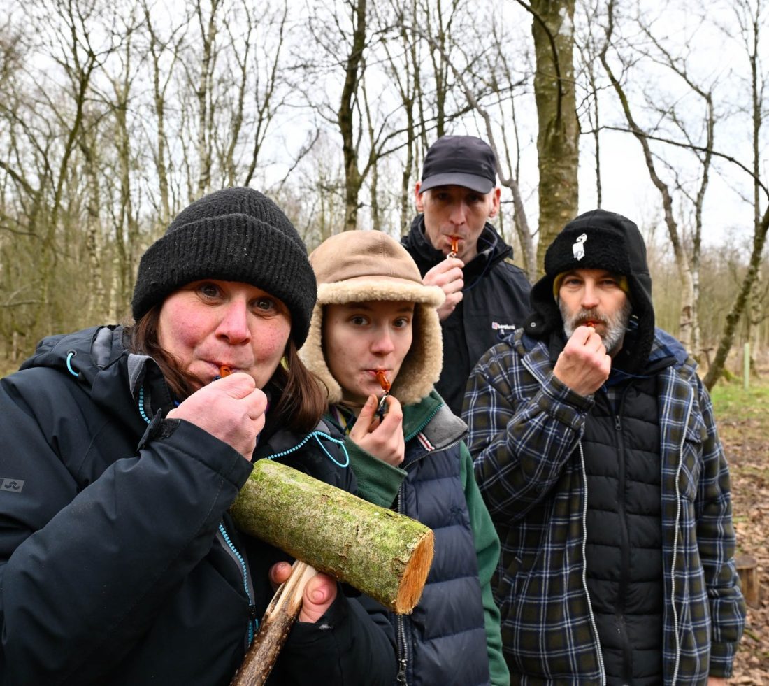 Four volunteers in the woods, blowing on wooden whistles, whittled on a volunteering celebration day.