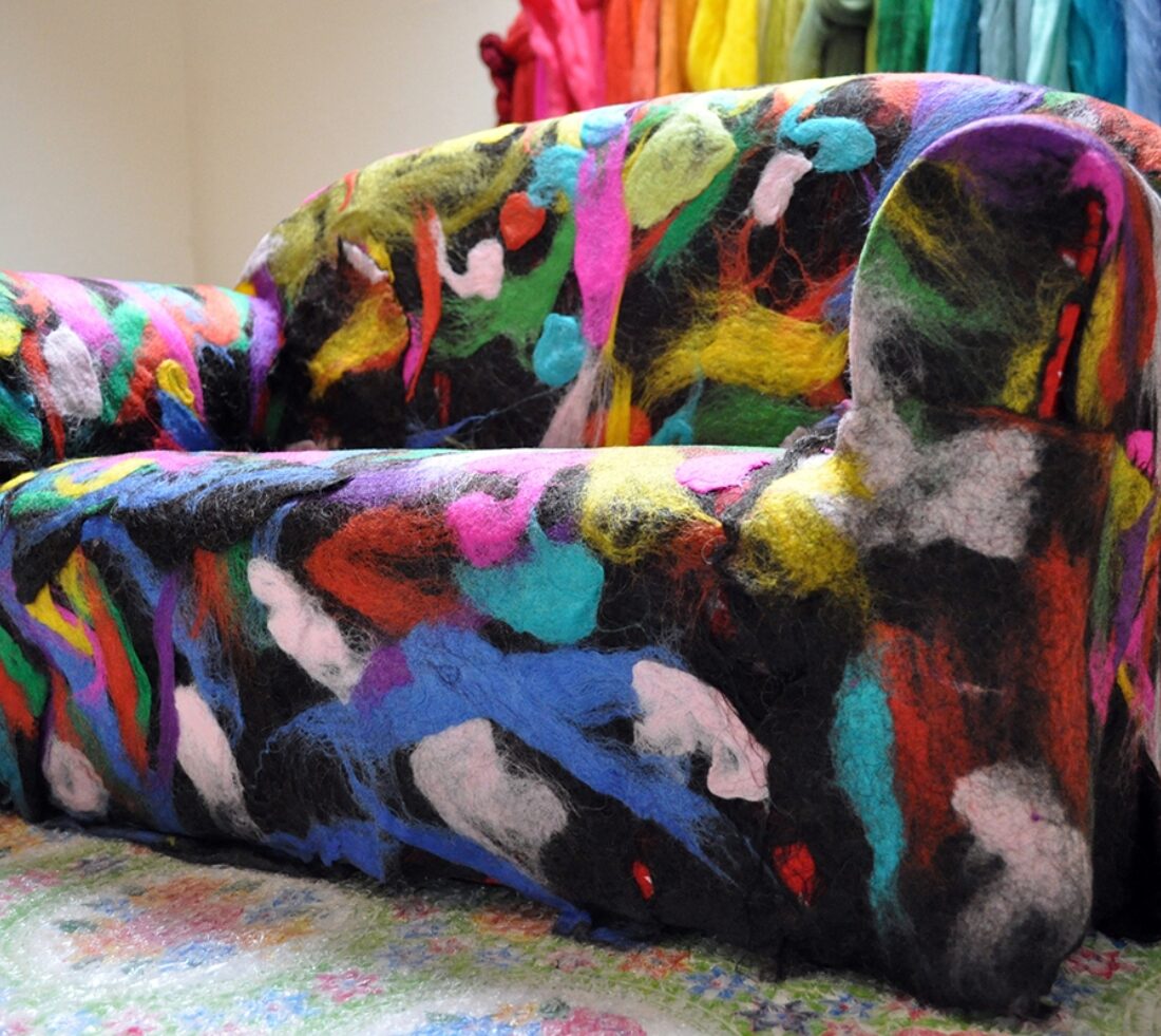 A large sofa has been covered in colourful felt design with black as its base colour, adorned with multicoloured felt splashes of colour.
