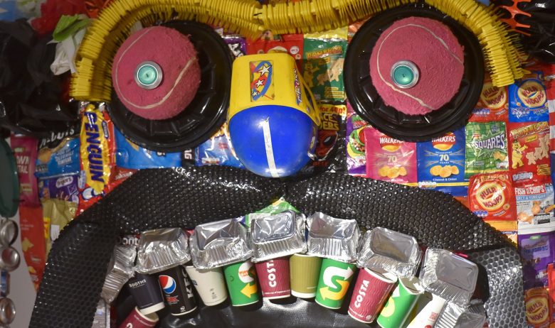 Close up view of a monsters face made from commonly found items of litter including foil trays and paper cups for teeth and empty crisp packets for skin.
