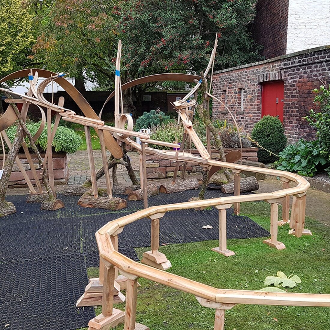 Outdoor photograph of a large wooden 'marble run' construction of a winding course supported by wooden legs.