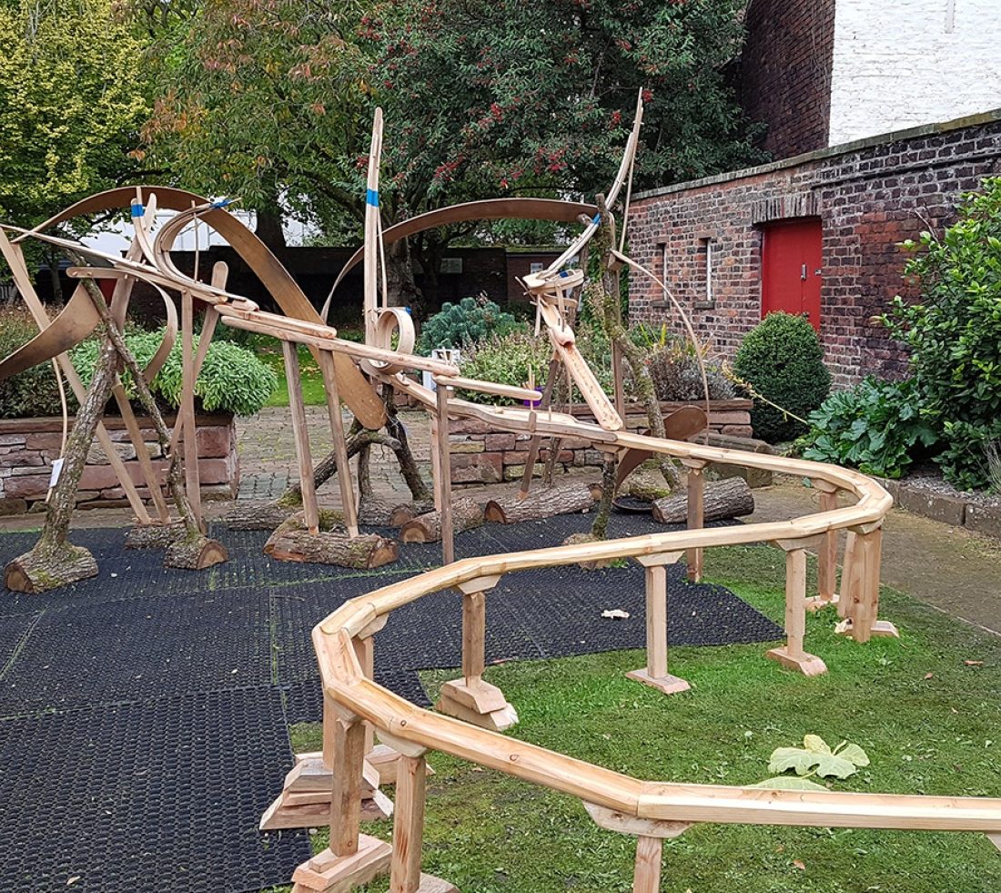 Outdoor photograph of a large wooden 'marble run' construction of a winding course supported by wooden legs.