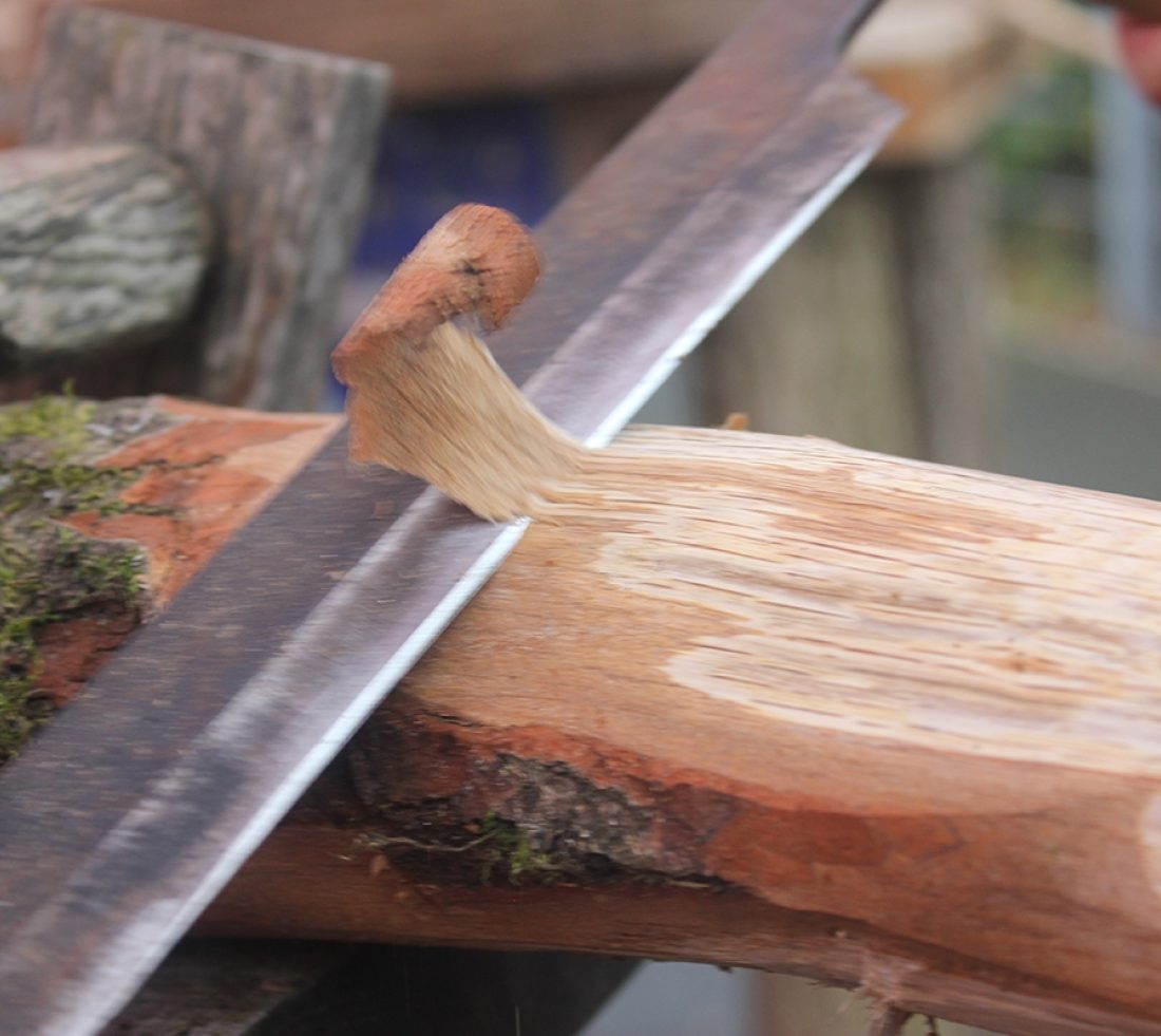 A section of wood being carved using the sharp edge of a wooden file.