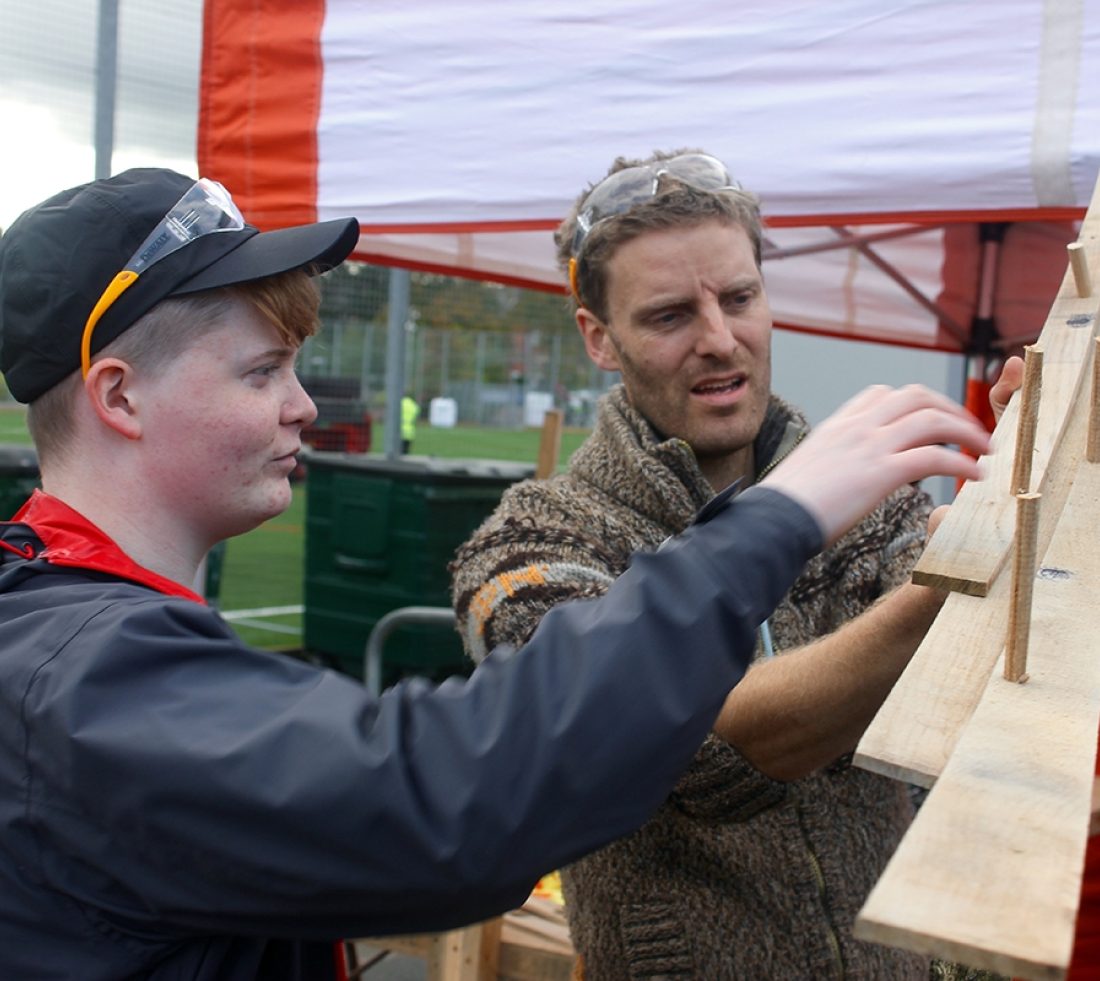 Two people holding a section of wooden marble run track.