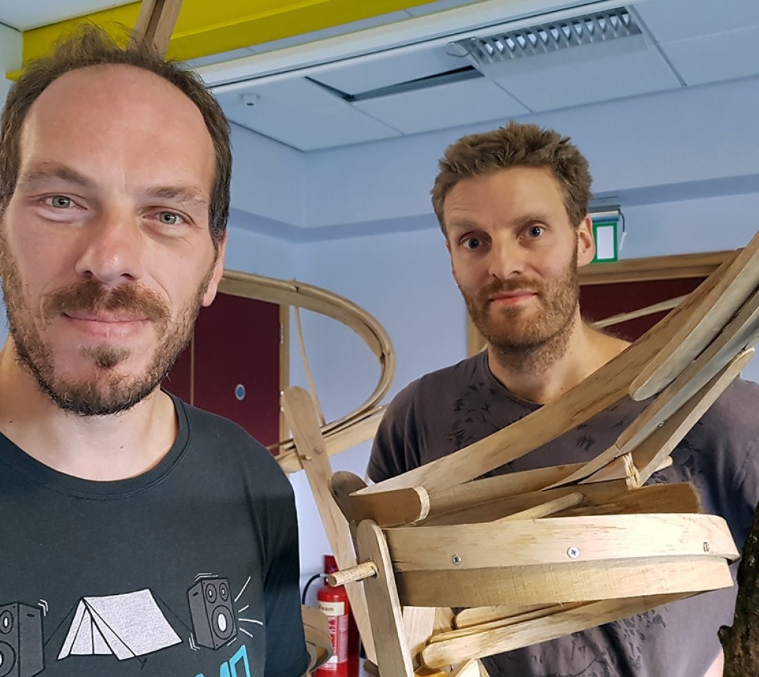 Two people posing for picture with a circular section of wooden marble run track.