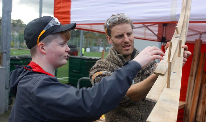 Two people holding a section of wooden marble run track.