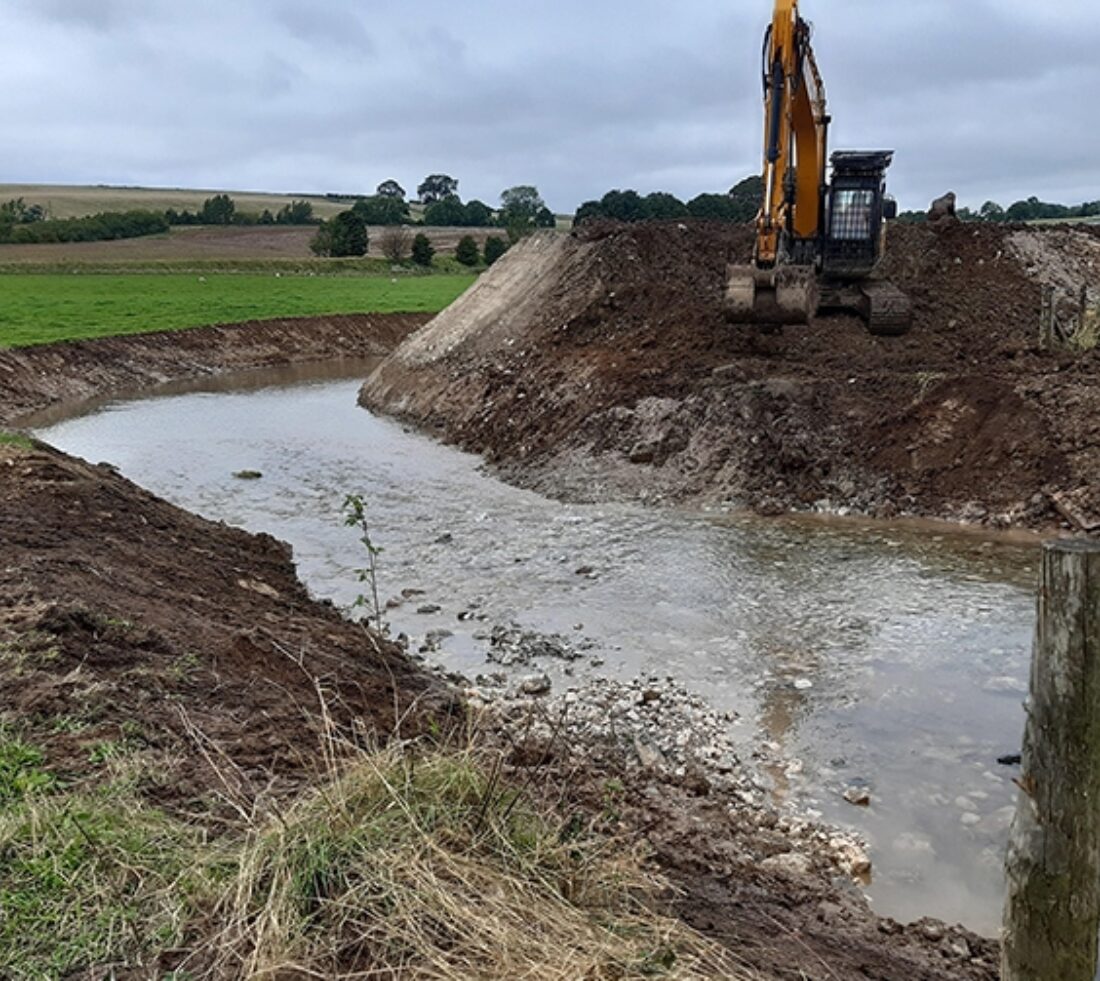 View across water channel to heavy plant machinery on opposite bank of excavated earth.
