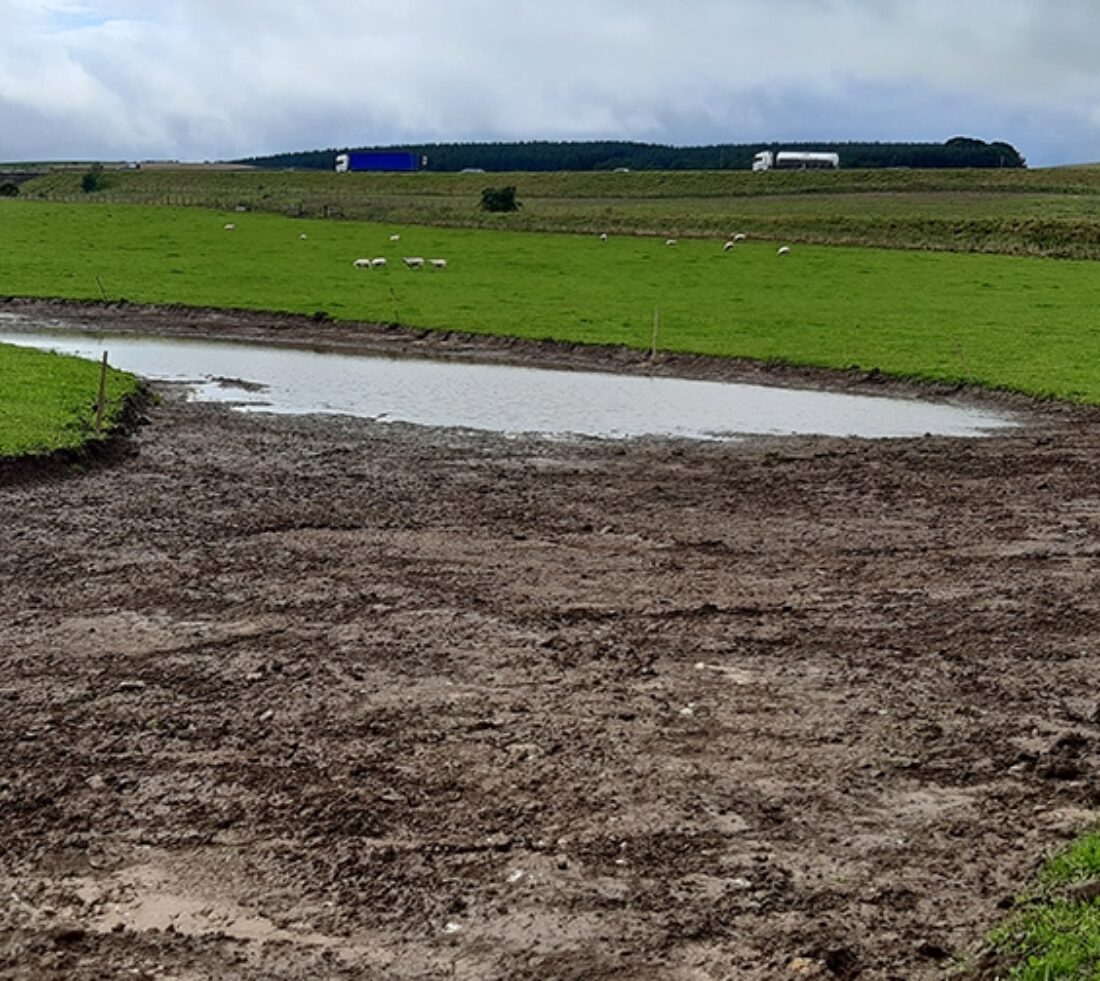 View across flat green field of a wide water channel excavation.