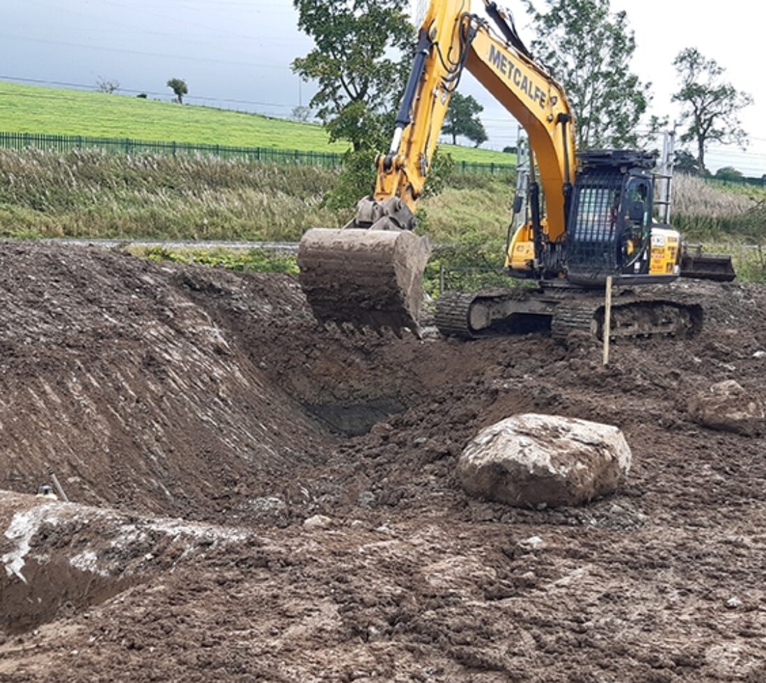 View across muddy soil excavation to heavy plant digger.