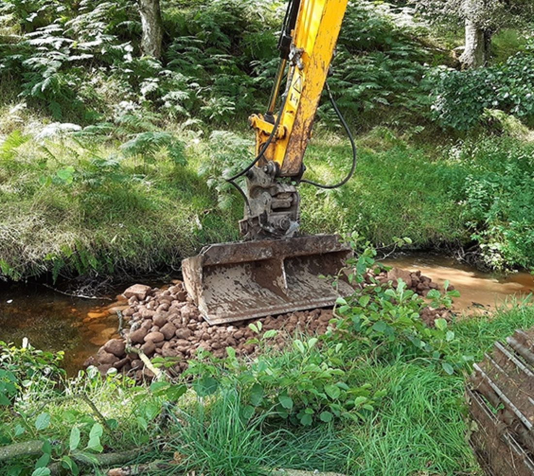 Digger bucket being used to create point bar in a river.