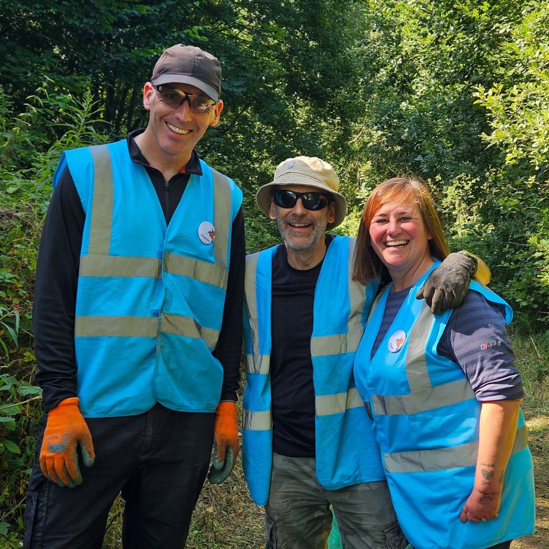 Three volunteers in blue hi vis jackets and orange gloves posing for a picture.