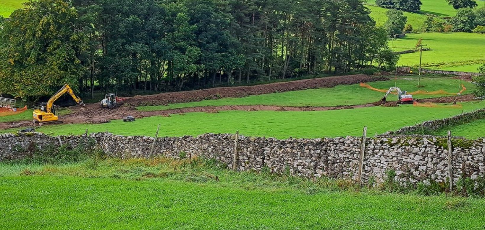 Diggers moving along narrow field channel to protect meadow beyond.