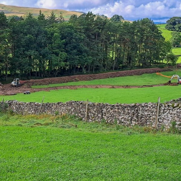 Diggers moving along narrow field channel to protect meadow beyond.