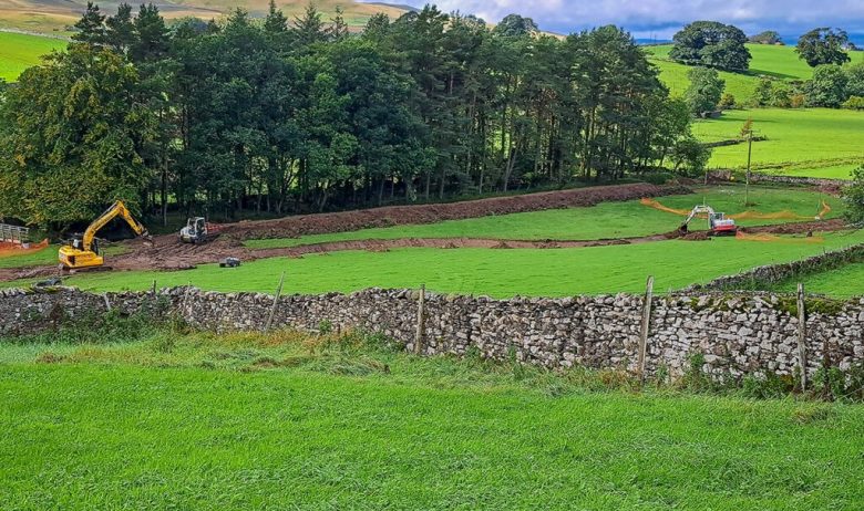 Diggers moving along narrow field channel to protect meadow beyond.