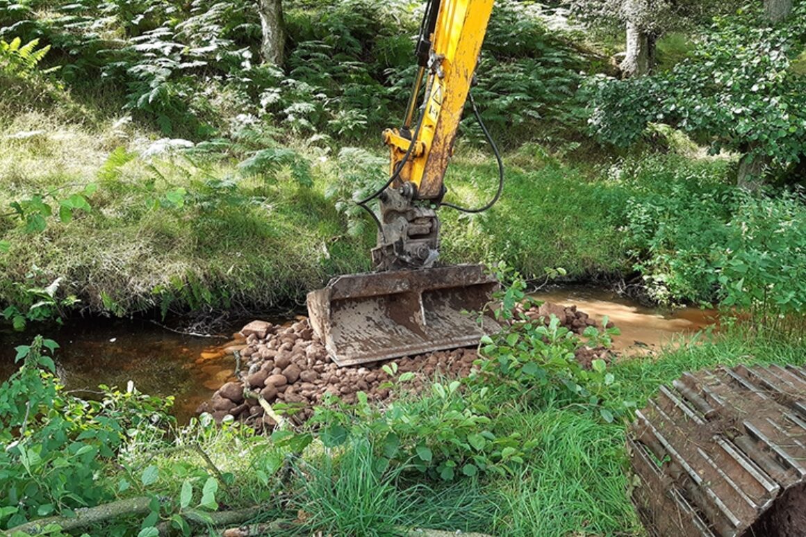 A JCB digger arm being used to create a point bar in the river