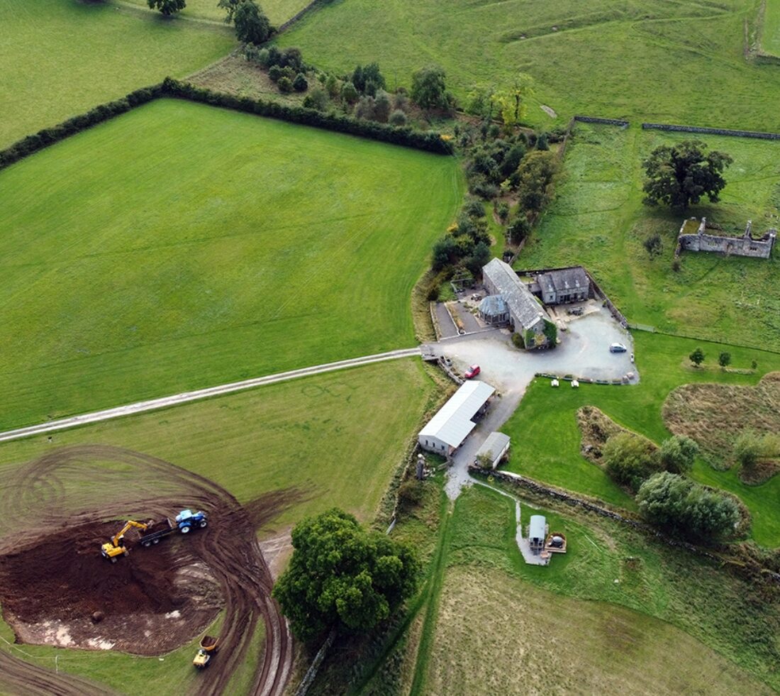 Aerial view of pond excavation in progress in front of large farmhouse.