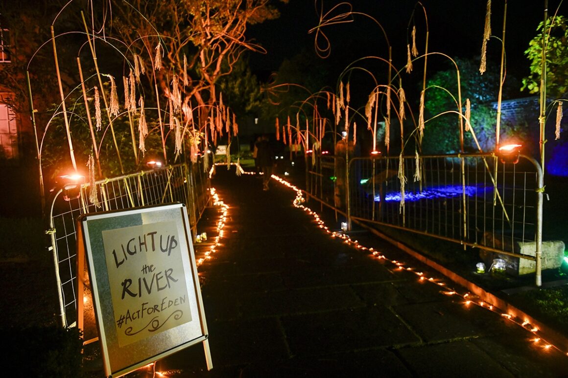 Looking down a pathway illuminated on each side with small orange lights with an A Board sign at its start which says: 