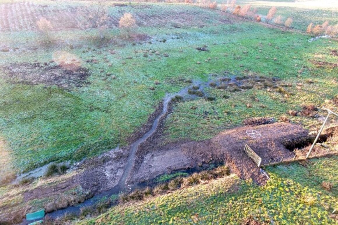 Aerial view of newly excavated river channel through grass field.