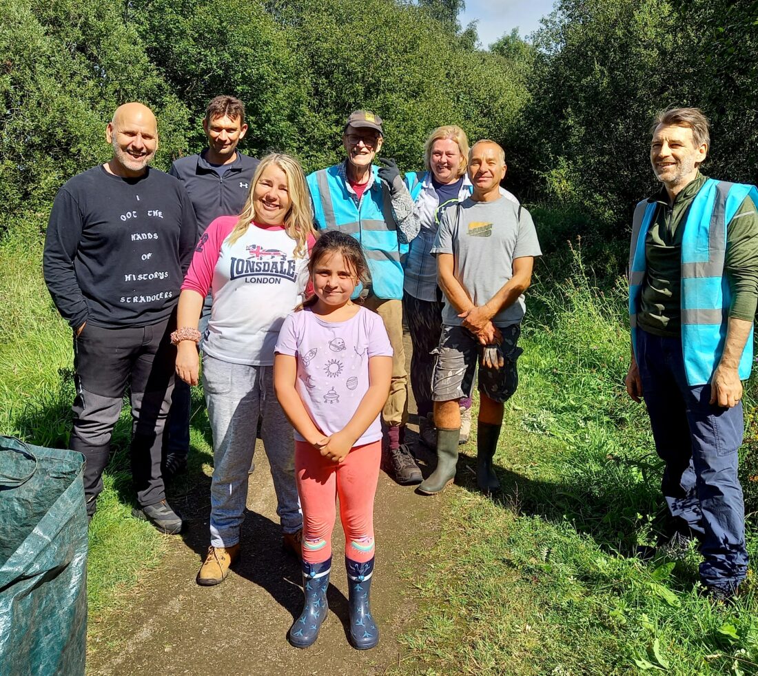 A group of Himalayan balsam bashing volunteers pose for a picture in sunshine.