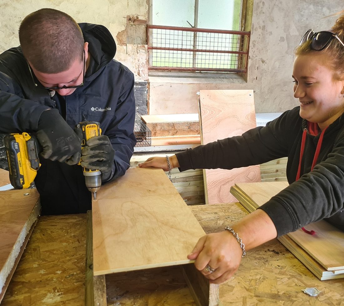 Students in a workshop drilling wooden panels in the construction of a mink raft.