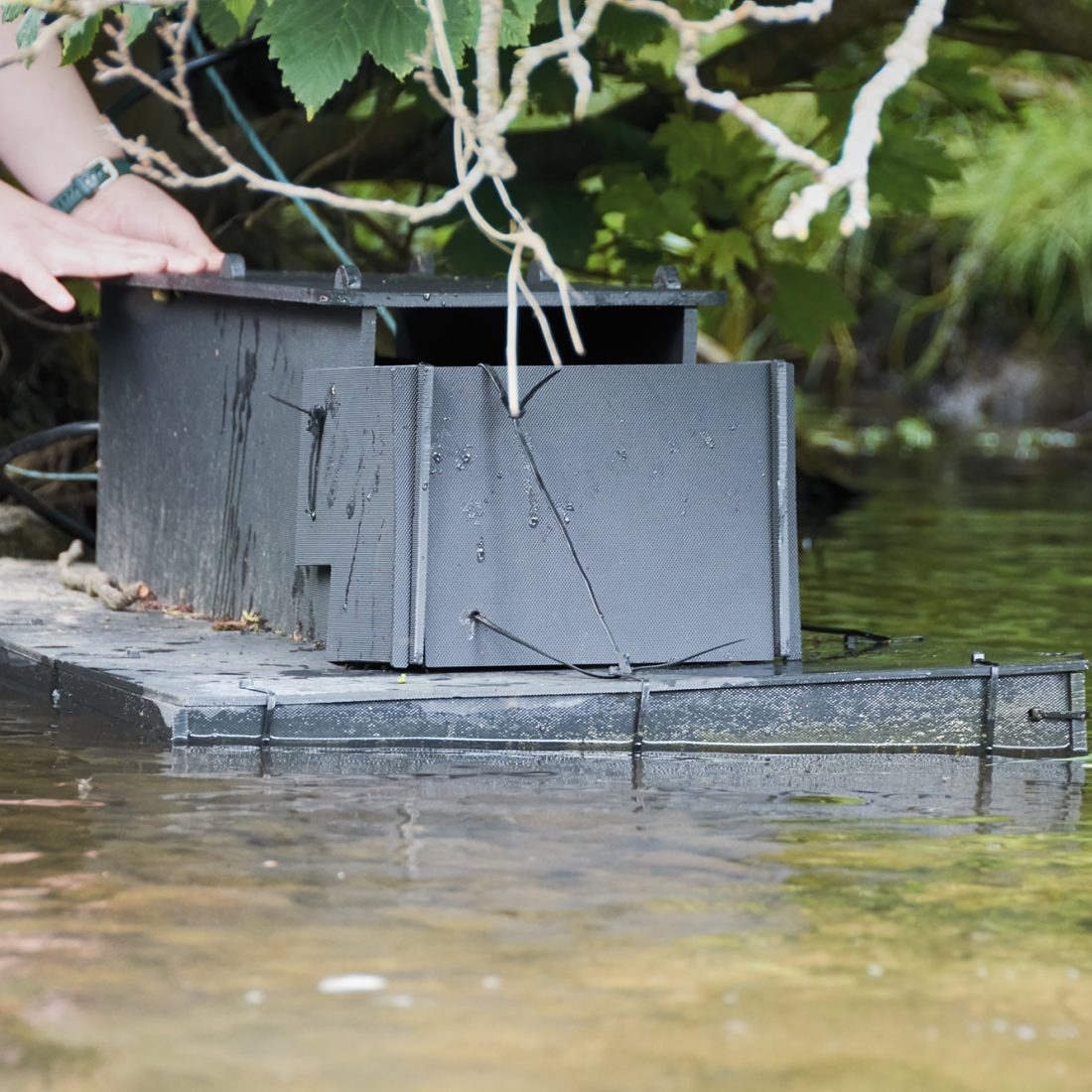 Grey box on top of a grey raft floating on water.