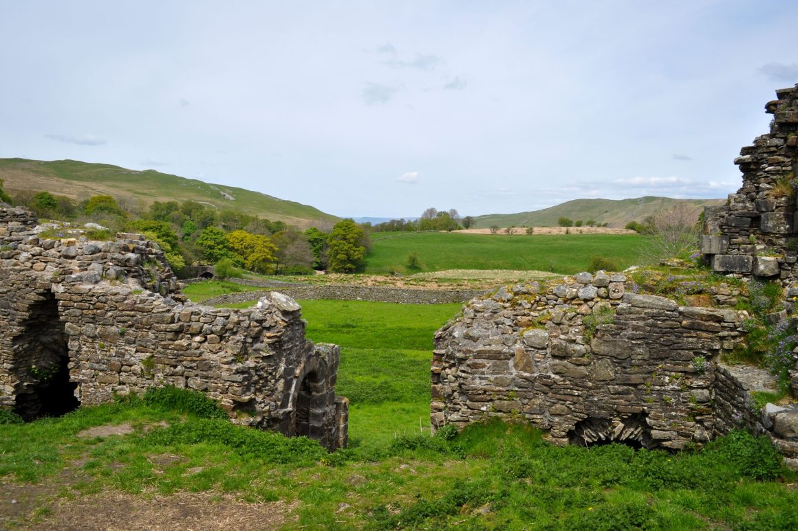 Derelict stone wall with gap through to green pasture beyond.