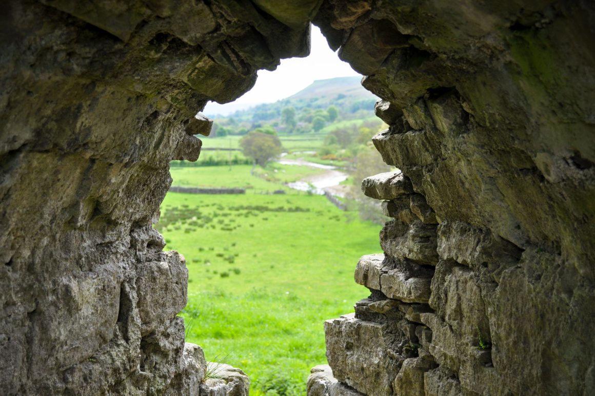 View through archway in thick stone wall to green pasture and meandering river.