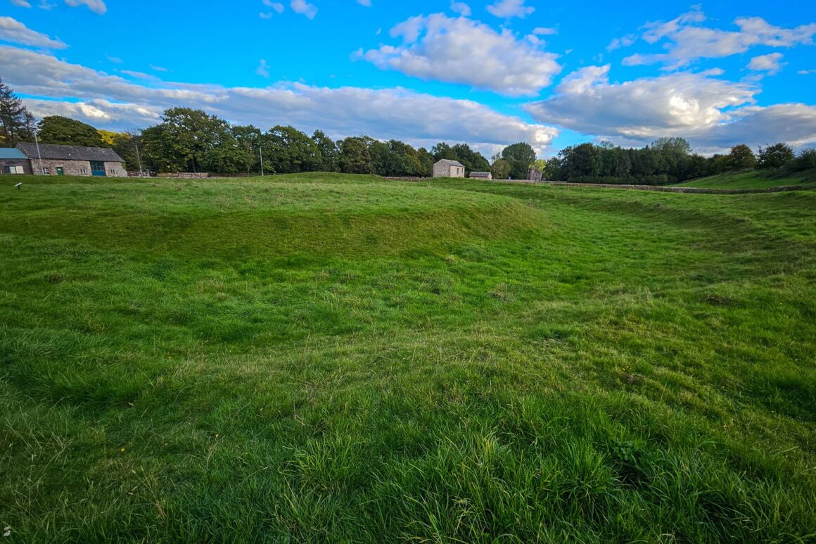 A grassy mound surrounded by a grassy moat in a field