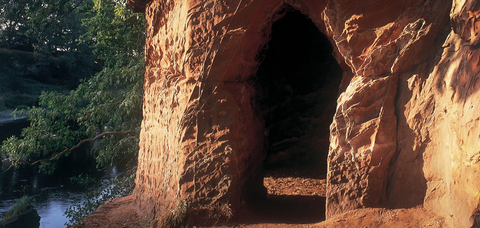 Carved out entrance to red sandstone caves on a cliff overlooking a river.