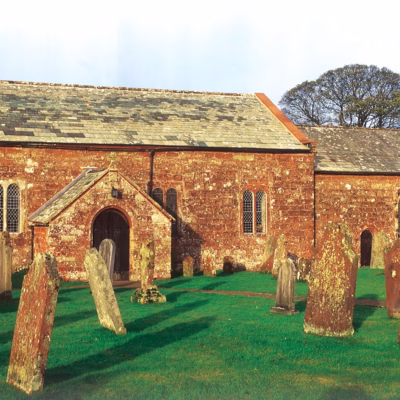 A brick church in a churchyard. There are a number of red stone gravestones in rows diagonally to the front of the church