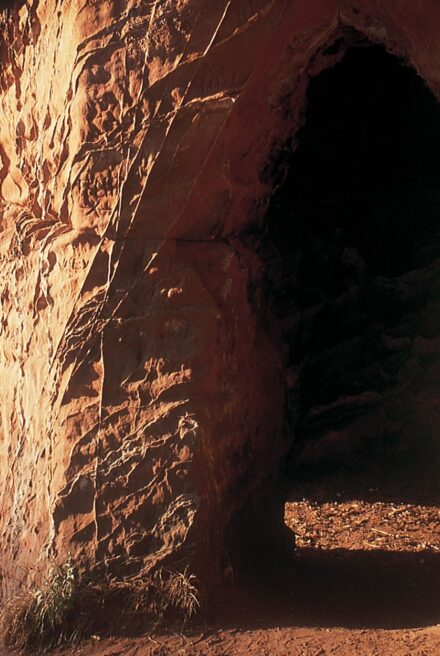 Carved out entrance to red sandstone caves on a cliff overlooking a river.