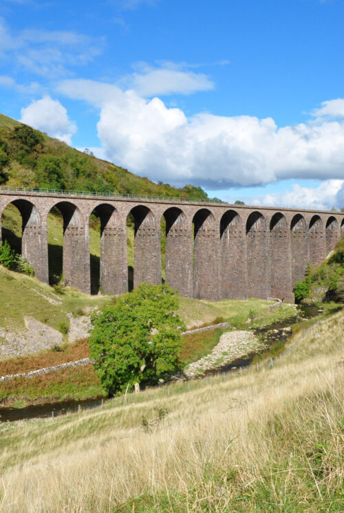Close up of Smardale Gill viaduct with its multiple sandstone arches. Scandal beck flows through and in front of the viaduct.