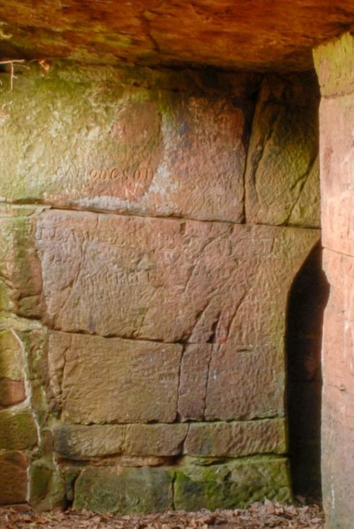 Passageway with a stone overhang that doesn't extend all the way across letting light in. To the right are two entrances to caves that have been carved out of the sandstone.