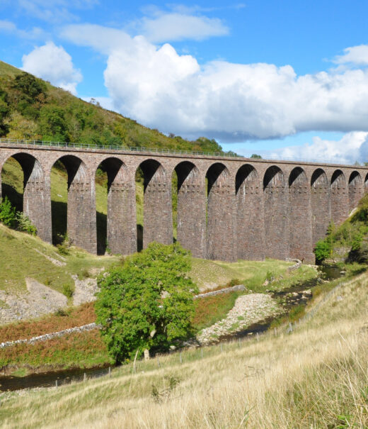 Close up of Smardale Gill viaduct with its multiple sandstone arches. Scandal beck flows through and in front of the viaduct.