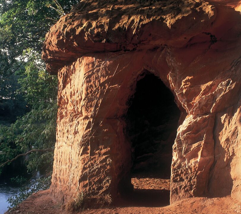 Carved out entrance to red sandstone caves on a cliff overlooking a river.