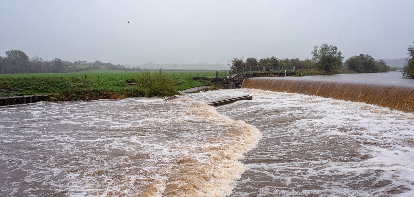 A view across the river Caldew in full spate cascading over Holme Head weir.