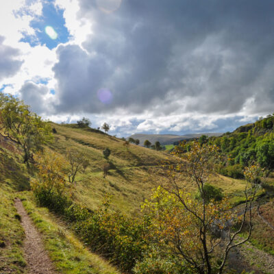 A steep valley with trees scattered along it. A river winds its way along the bottom of the valley