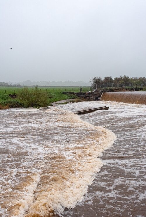 A view across the river Caldew in full spate cascading over Holme Head weir.