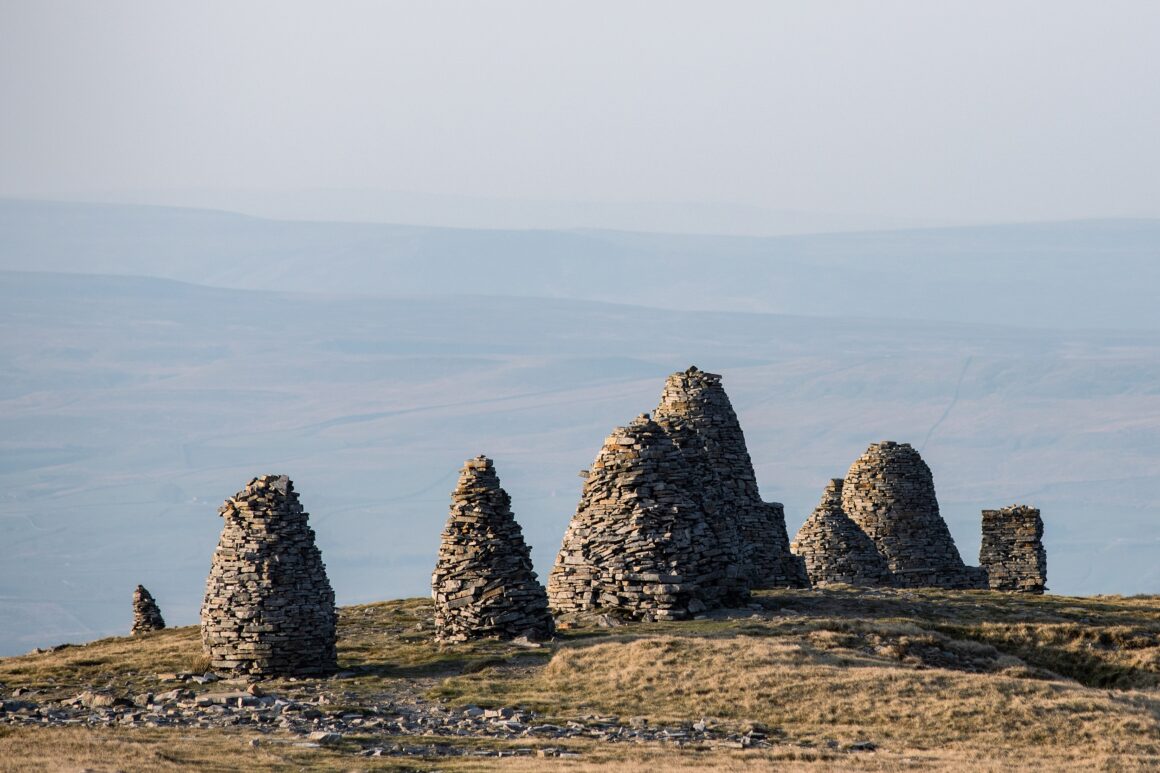A group of nine very tall stone cairns, all of different sizes, stand in a line on the top of a hill.