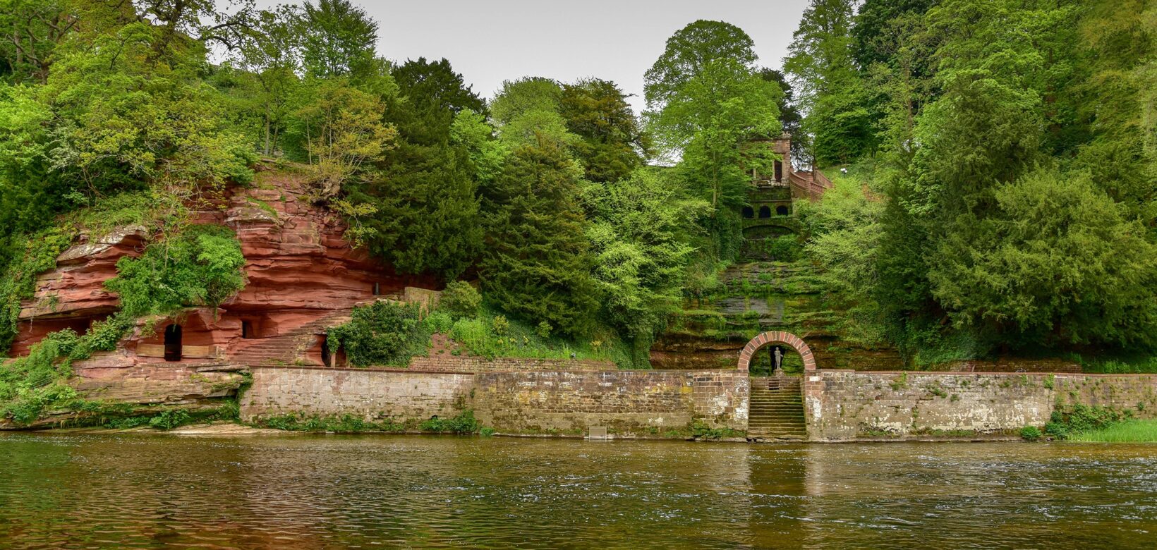 Across the River Eden, cut into the hillside lies Corby cascade, a waterfall behing a stone wall and gate and caves carved into red standstone.