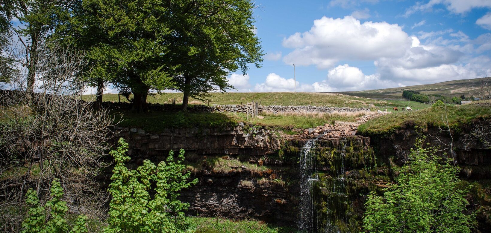 Water run off from fields cascading over high river bank into small gorge.