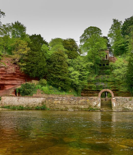 Across the River Eden, cut into the hillside lies Corby cascade, a waterfall behing a stone wall and gate and caves carved into red standstone.