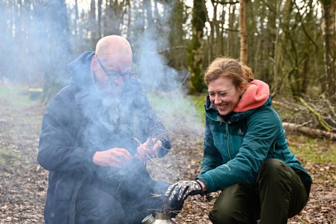 Volunteer and ERT staff member adding kindling to a metal fire pot.